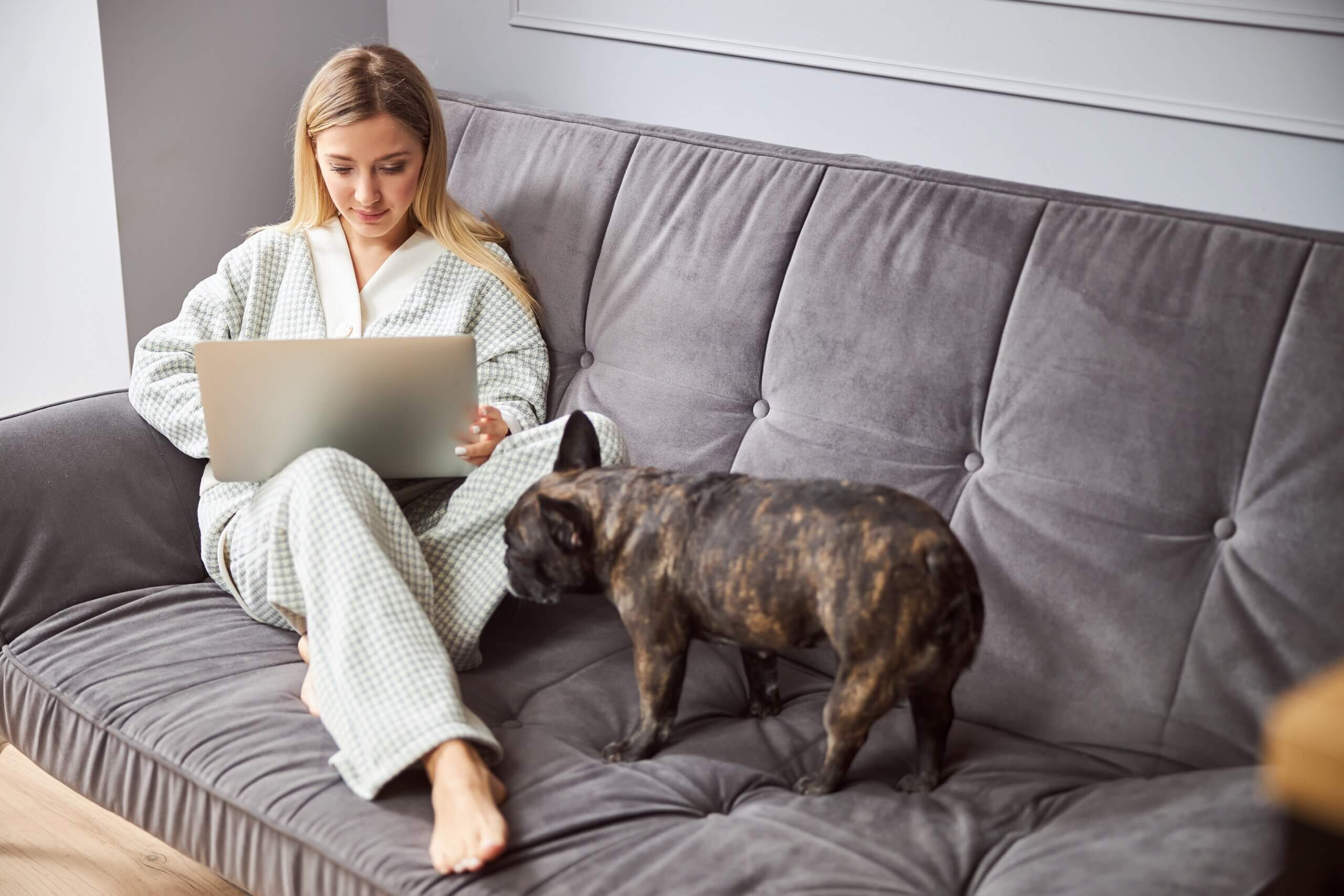 A woman working from her couch with her dog nearby.
