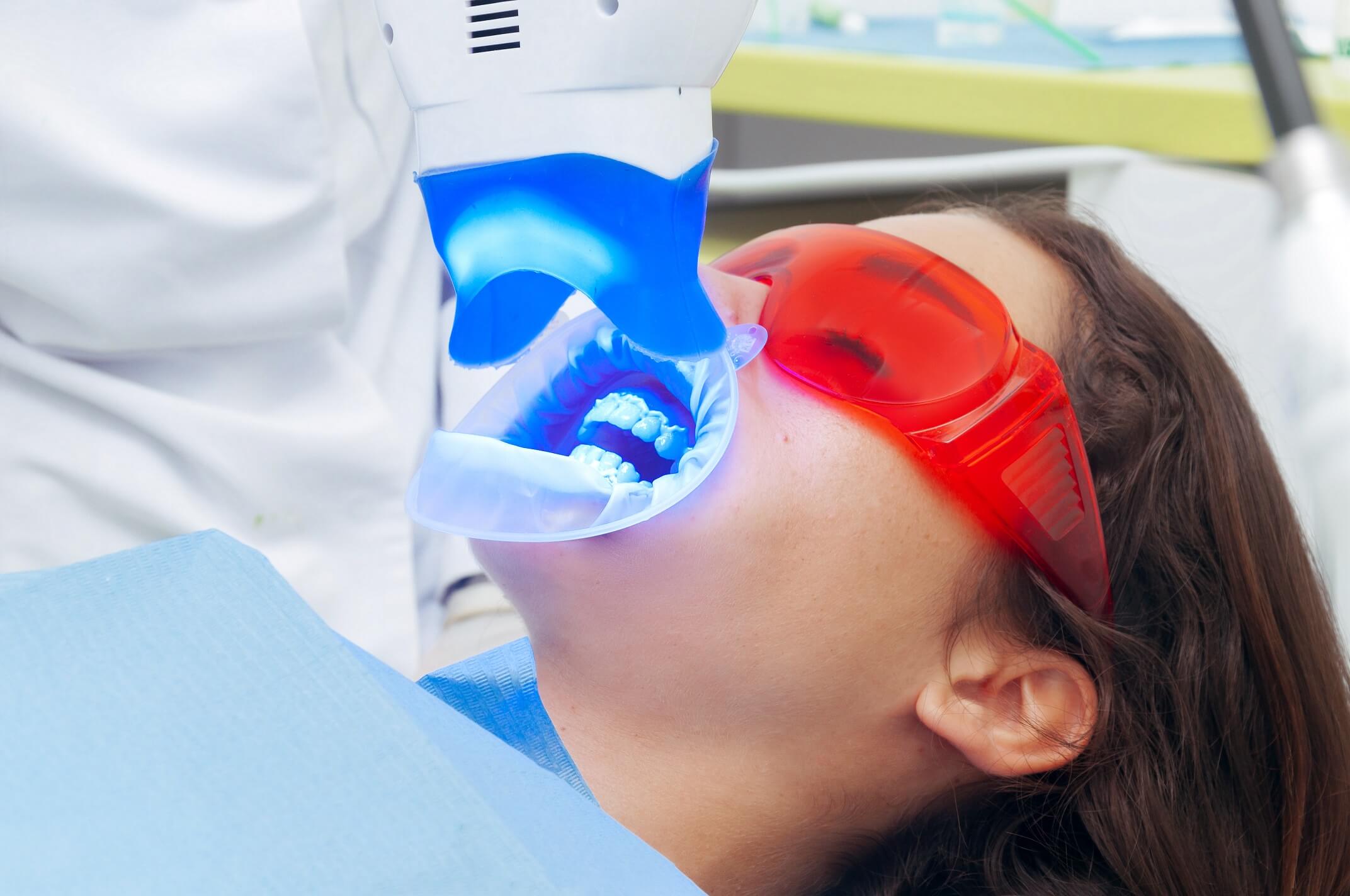 A machine shining a bright blue light on a girl's teeth while she sits in a dentist chair.
