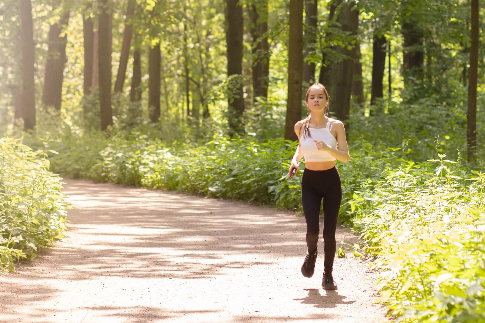 Teini-ikäinen tyttö juoksee polulla metsässä.