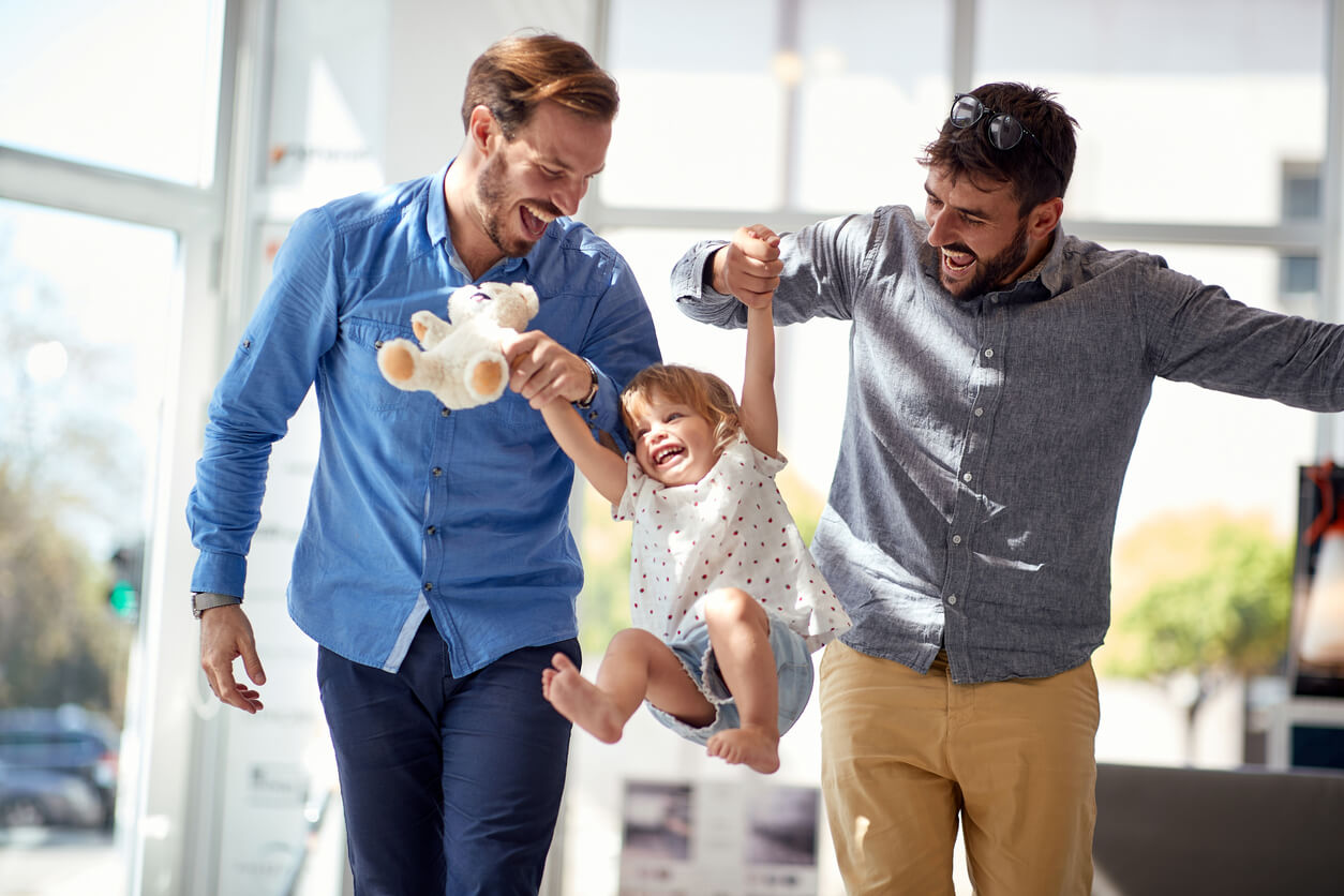Two adoptive dads swinging their toddler daughter in the air.