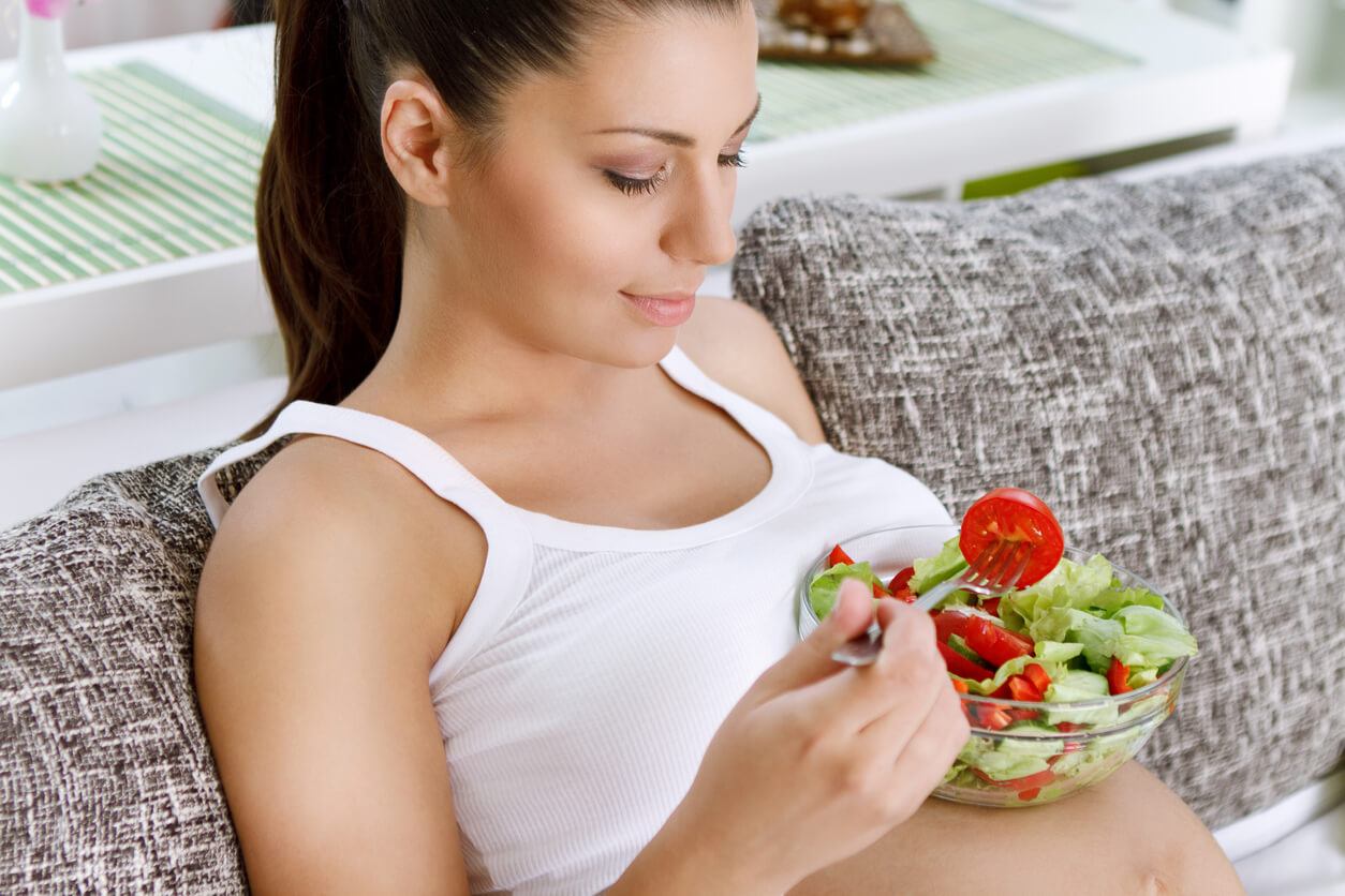 A pregnant woman eating a salad that contains tomatoes.