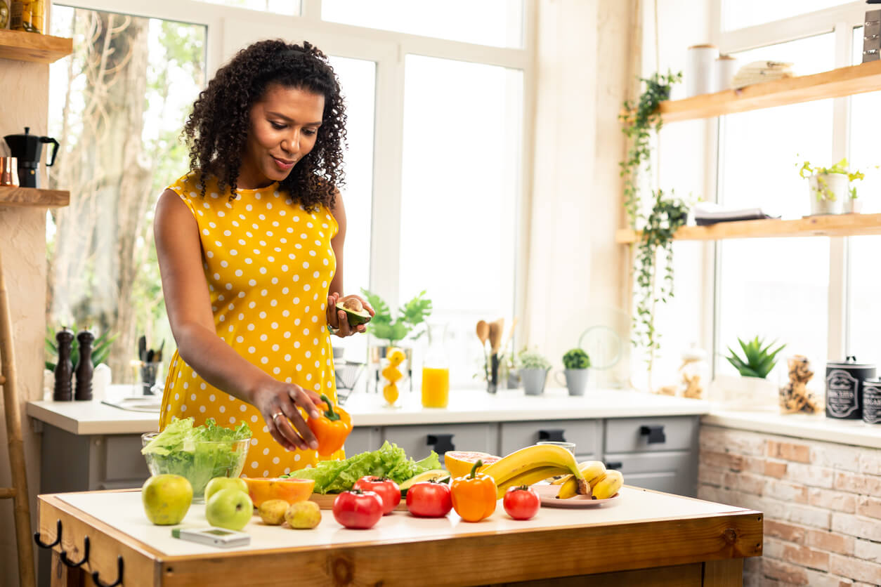 En kvinna som ställer färsk frukt och grönsaker på köksbänken.