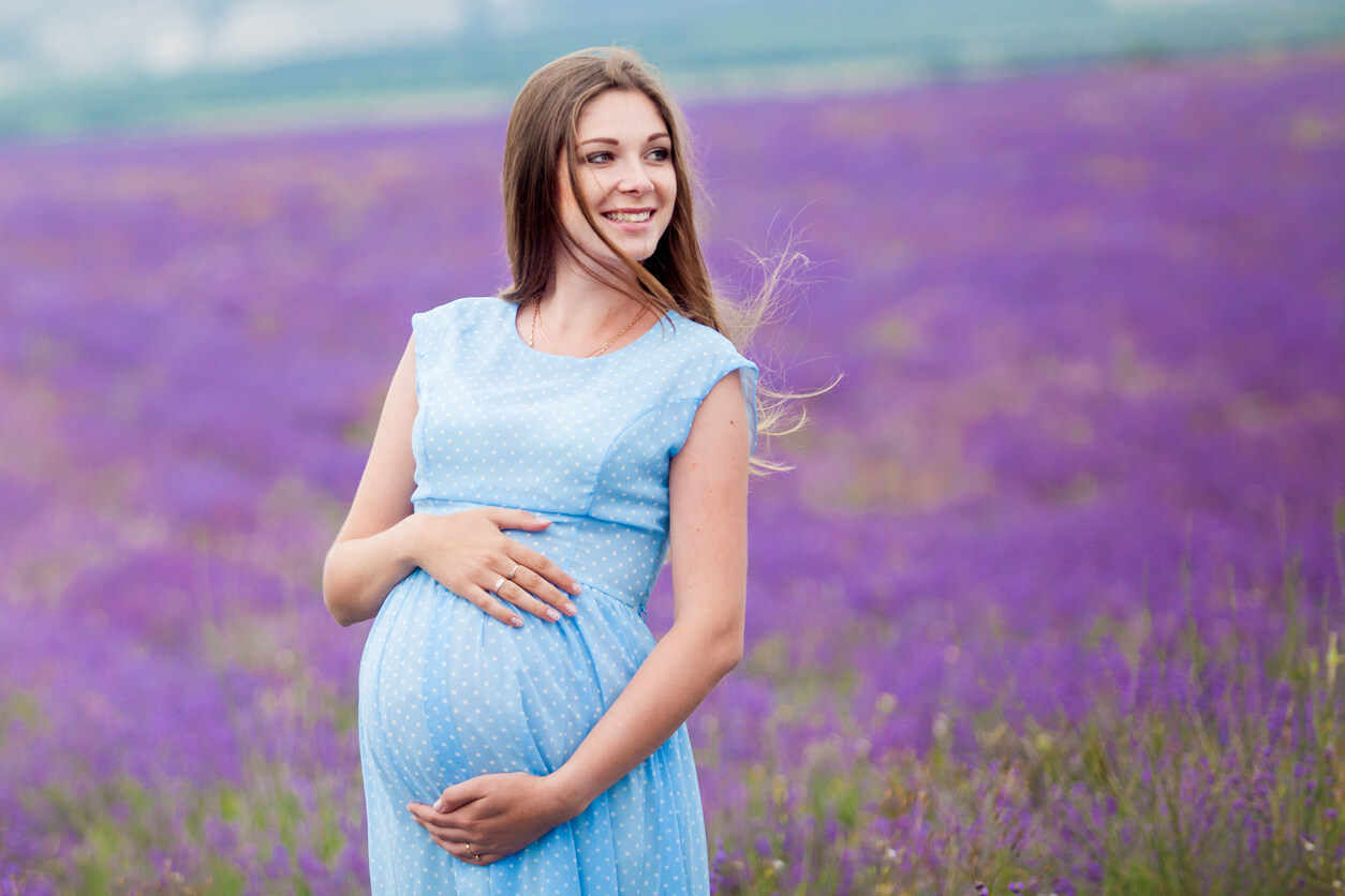A pregnant woman wearing a light blue dress and standing in a field of lavender.