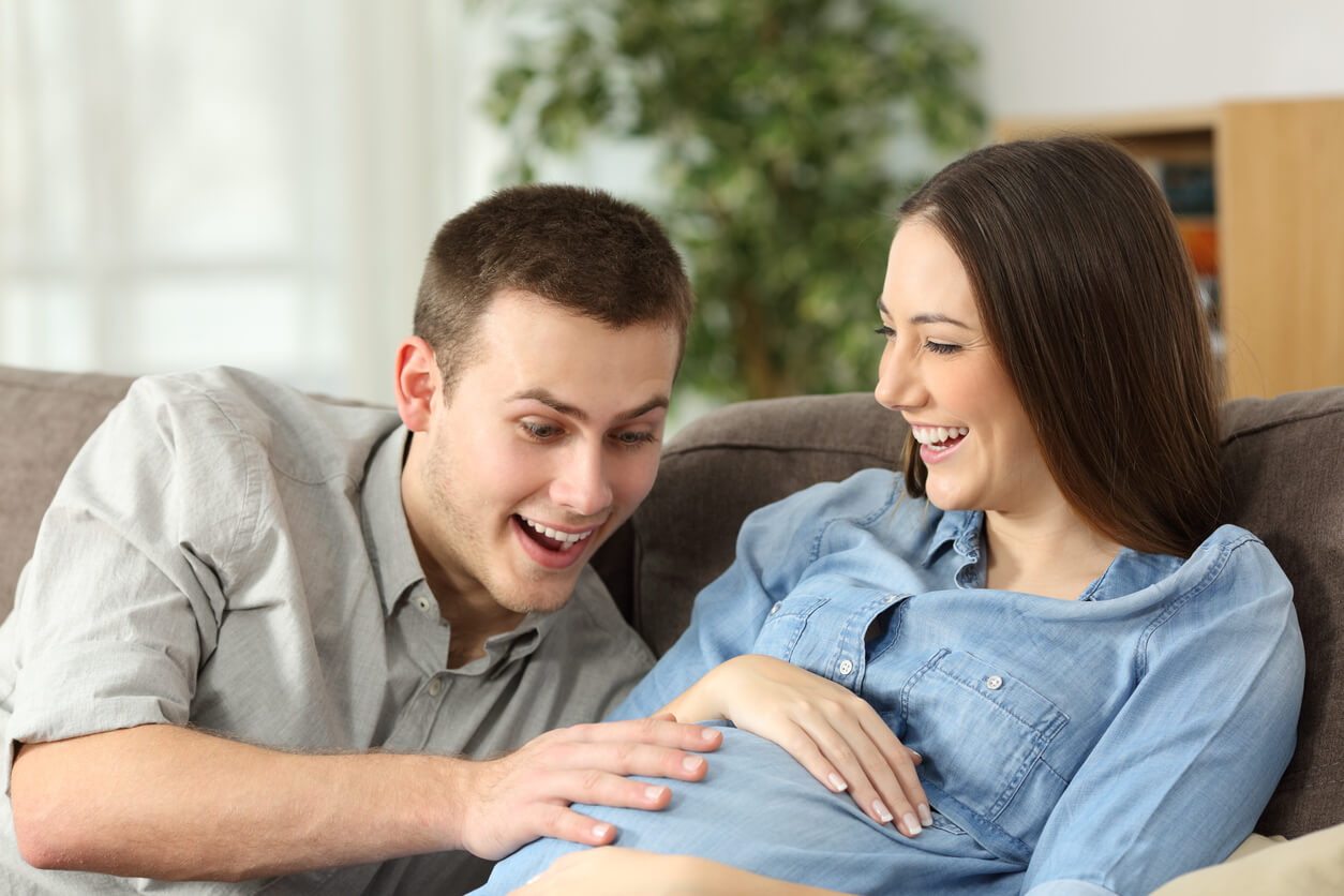 Un couple qui s'amusent à sentir les mouvements du bébé dans le ventre de la femme enceinte. 