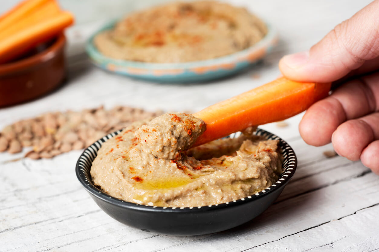 A person dipping a carrot in hummus.