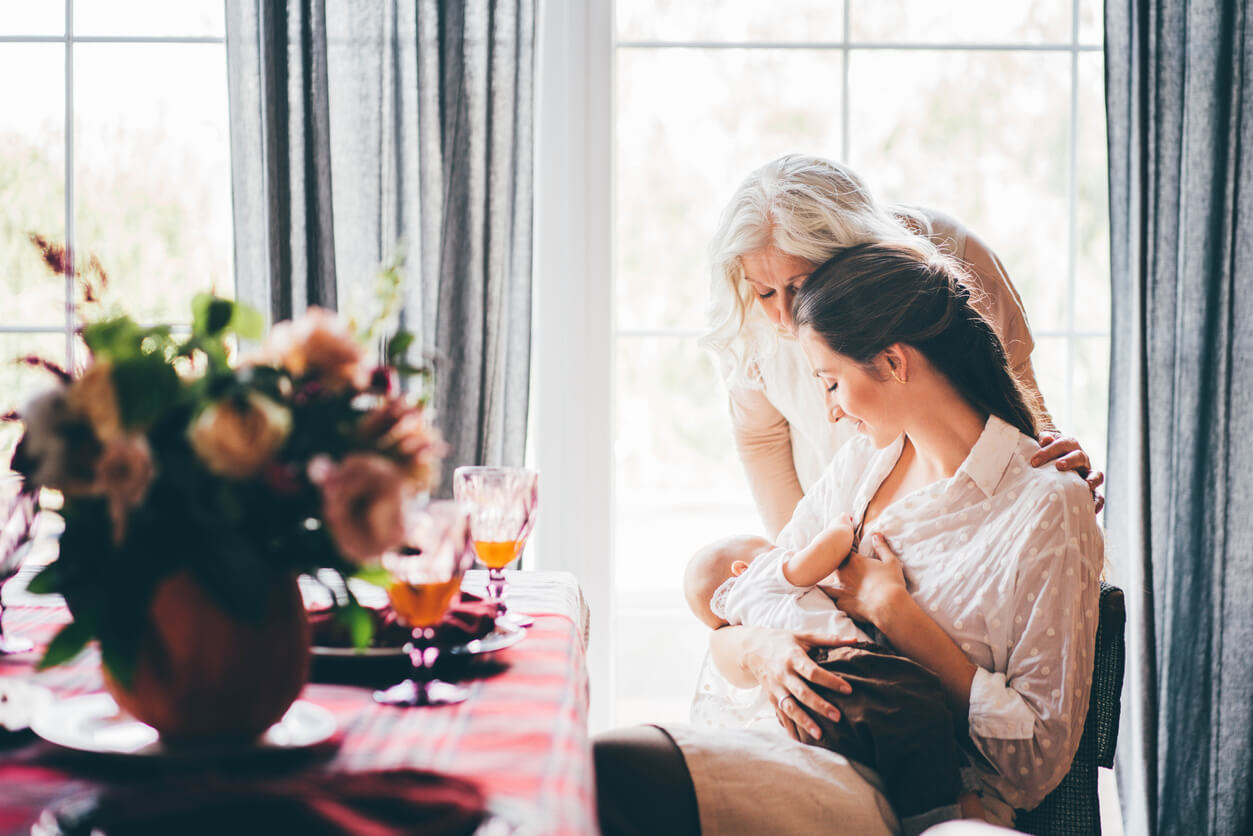 A mother breastfeeding her baby at the dining room table.