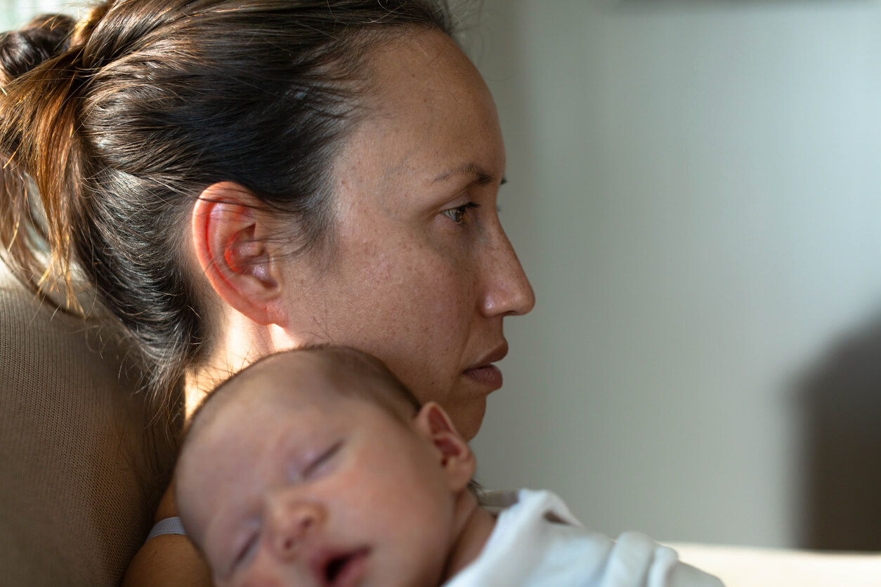 A mother with a blank look on her face holding a newborn.