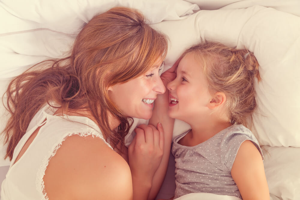A mother and daughter laughing in bed.