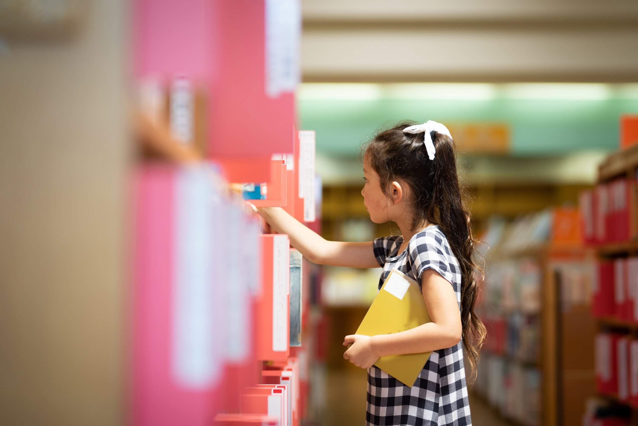 A young girl looking at books on a library shelf.