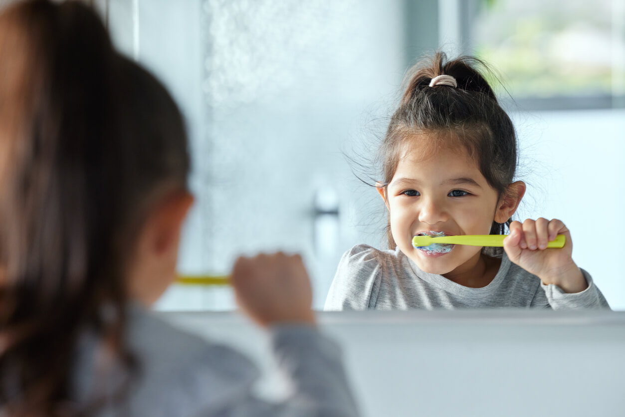 En liten flicka tittar i spegeln och borstar tänderna.