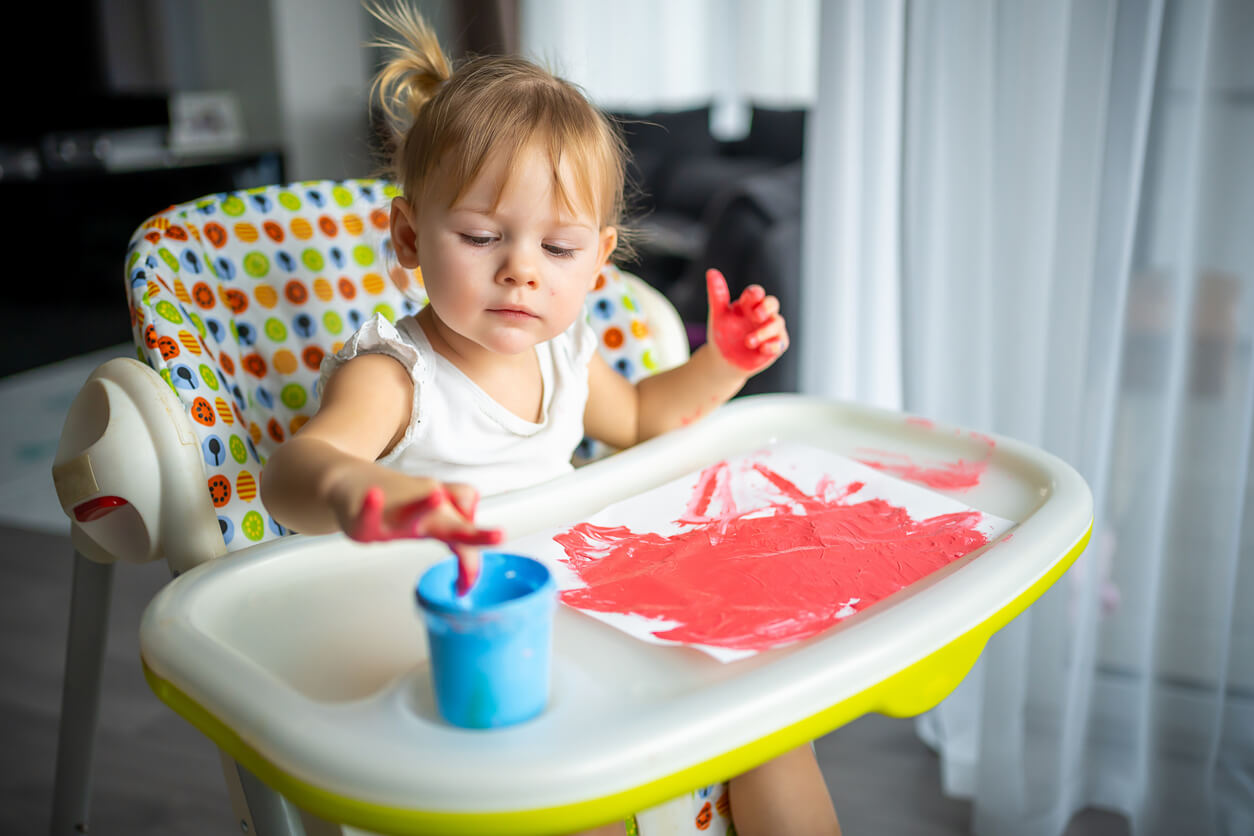 A toddler girl finger painting in her high chair.