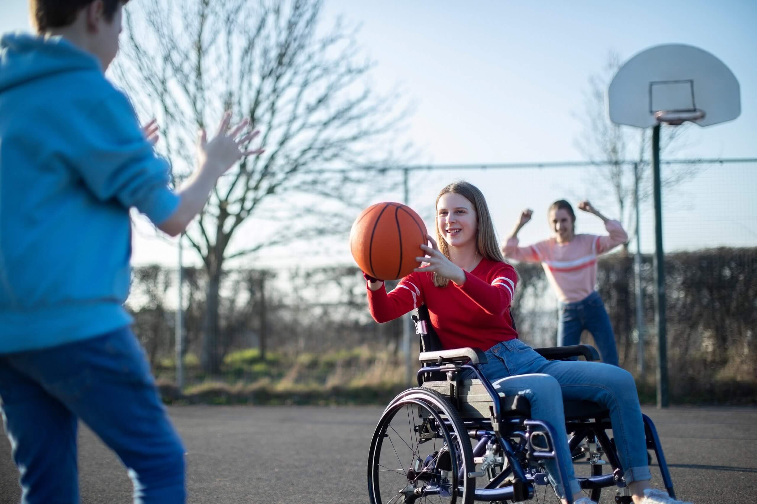 Several teens playing basketball, one of whom is using a wheelchair.