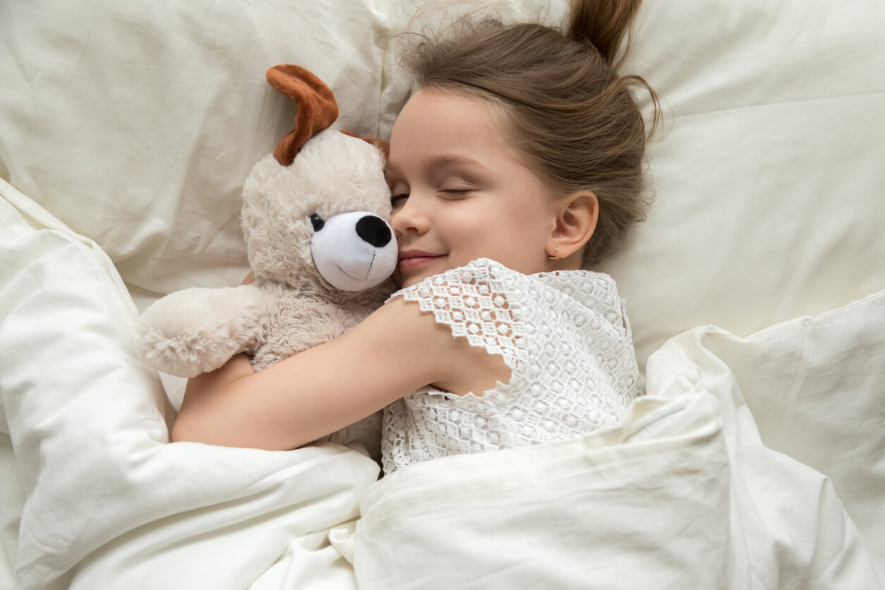 A little girl sleeping while snuggling her teddy bear.