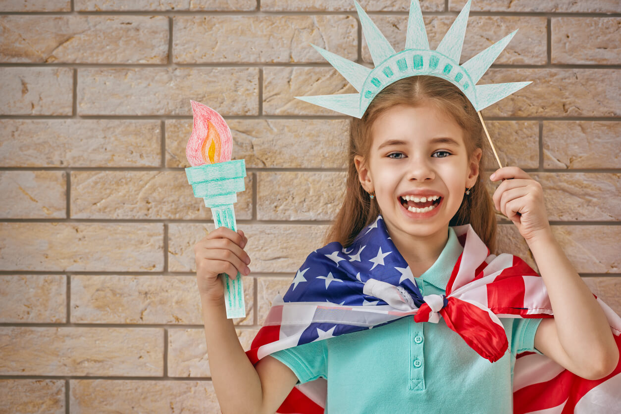 Vapaudenpatsaaksi pukeutunut tyttö Yhdysvaltain lippu olkapäillään.
