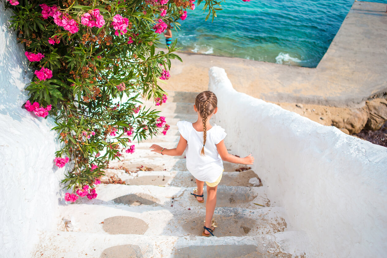 A little girl walking down a white staircase near the sea in Greece.