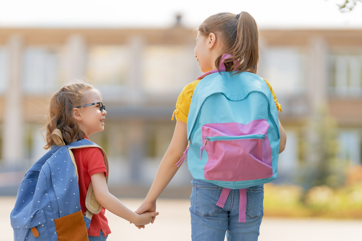 Two sisters walking into school wearing backpacks.