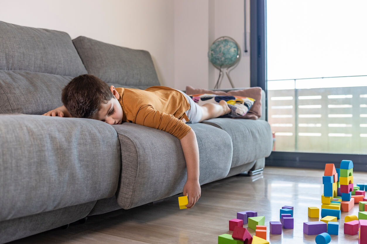 A bored child lying on the couch looking at his blocks.