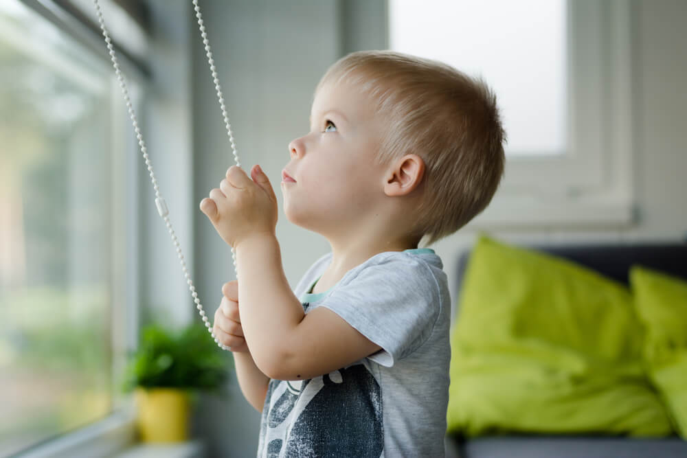 A toddler raising the blinds in his room.