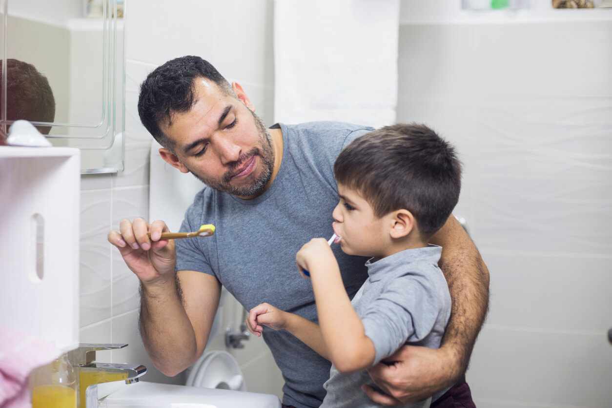 A father helping his son brush his teeth.