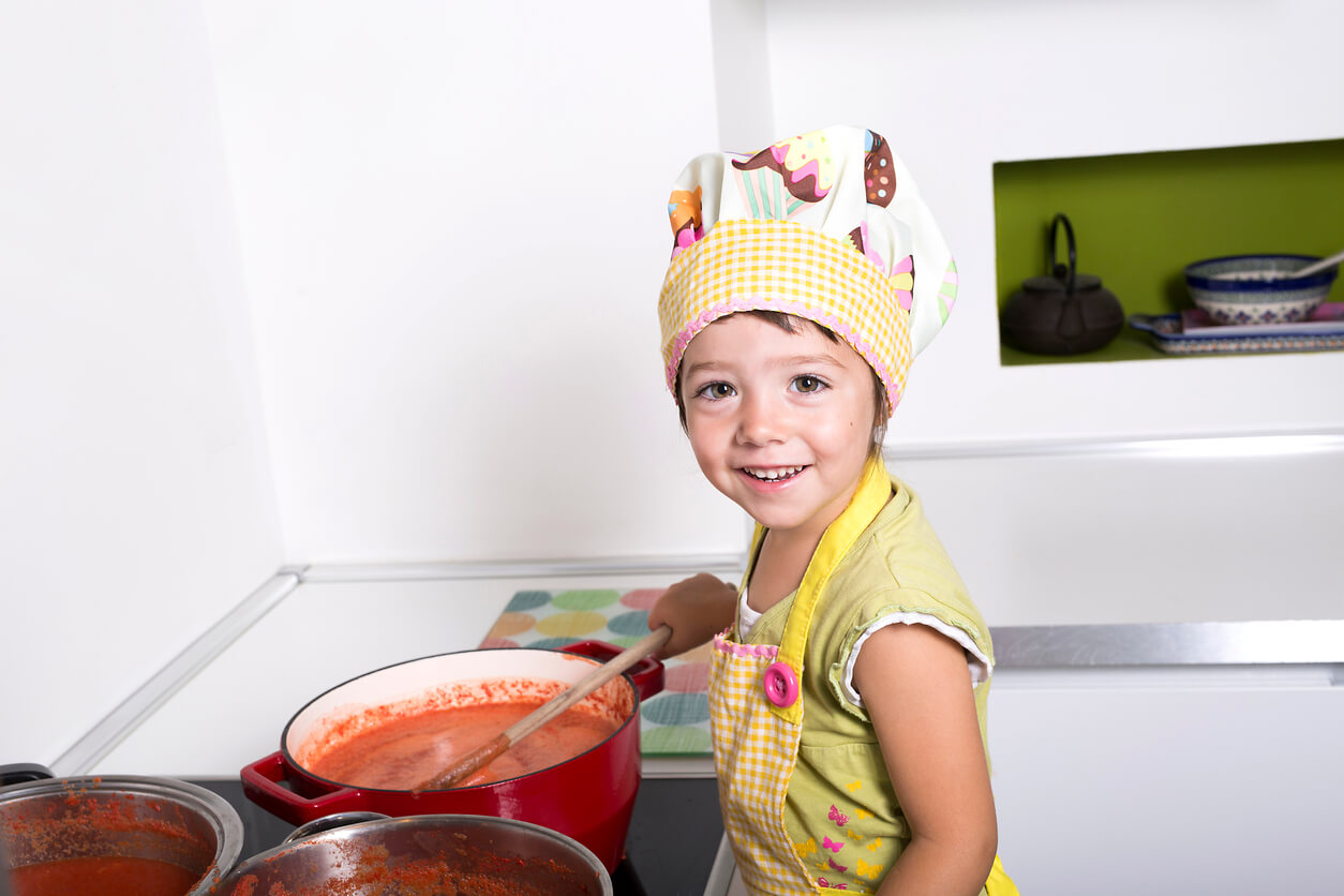 A child stirring a pot of tomato sauce on the stove.