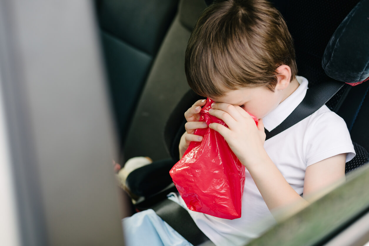 A child in a car throwing up into a plastic bag.