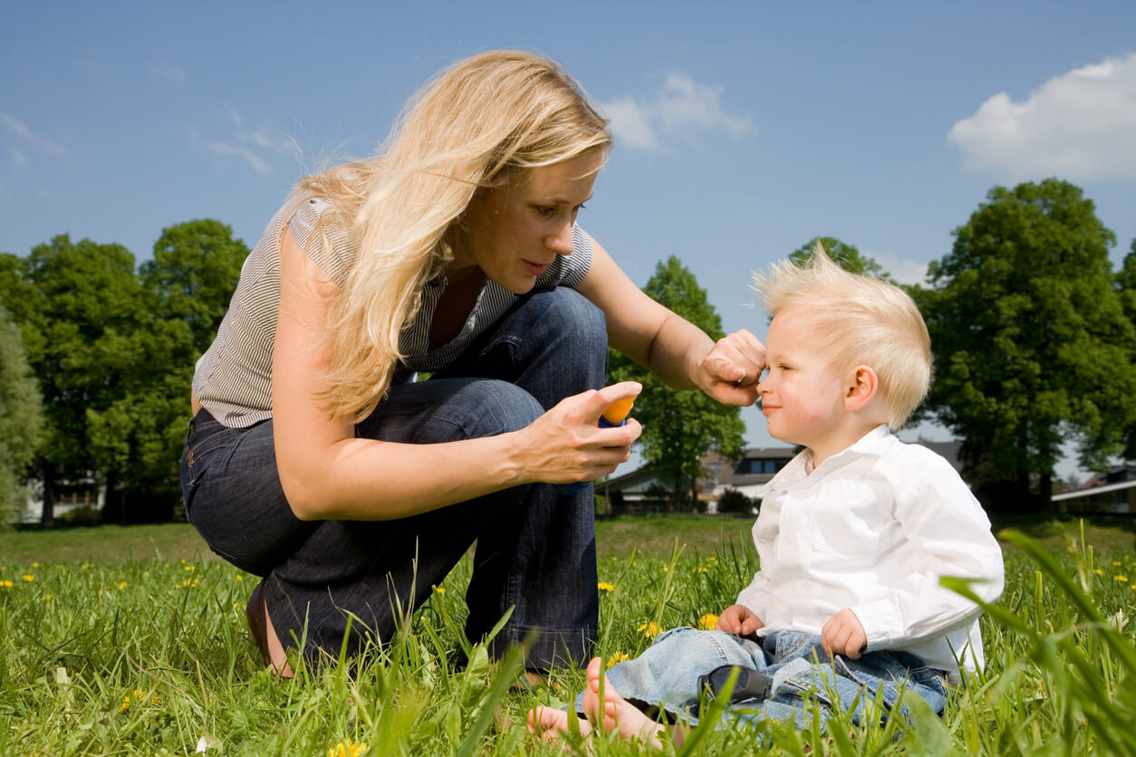 A mother applying sunscreen to her son's face while sitting in the grass.