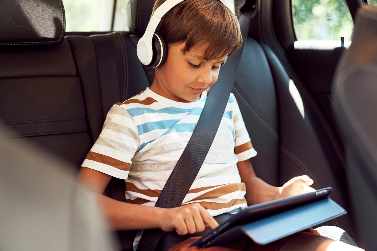 A child listening to headphones and using a tablet while riding in the car.