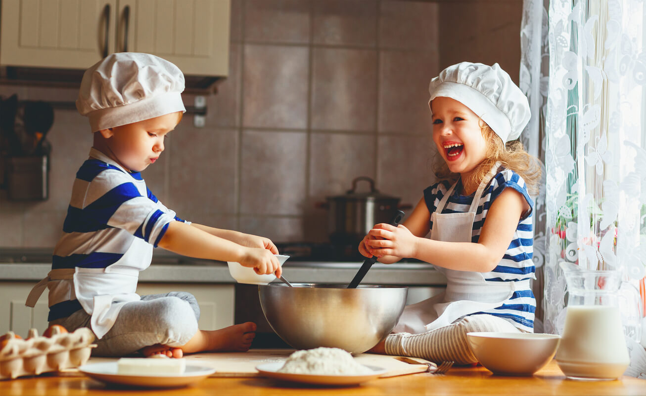 Two young children sitting on the counter mixing ingredients in a bowl.