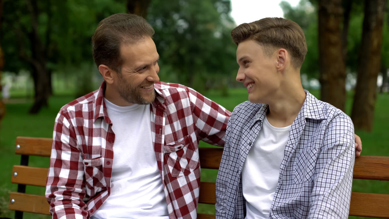A father and his teenage son having a positive conversation on a park bench.