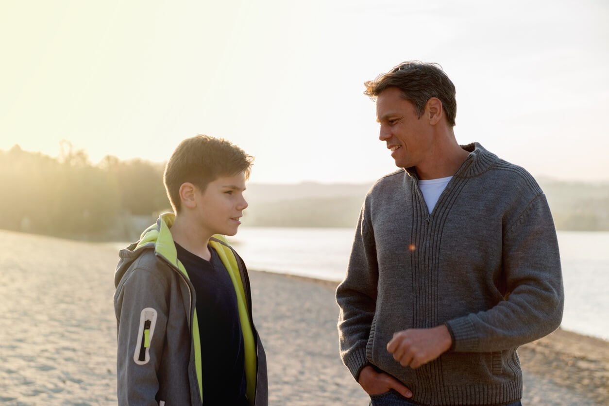 A father and his preadolscent son talking on the beach.