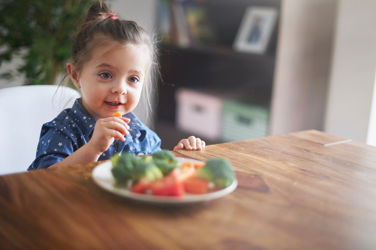 A toddler girl eating vegetables.