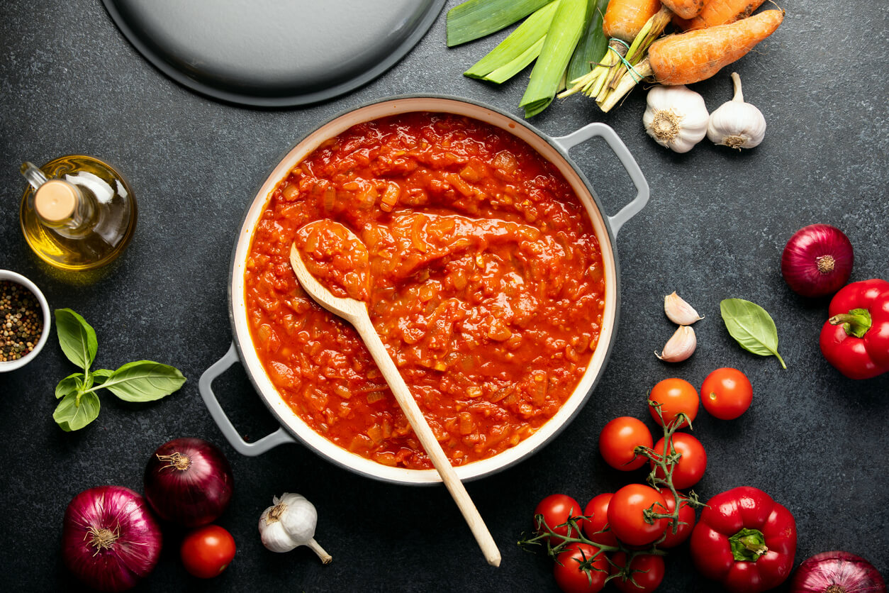A pot of homemeade tomato sauce surrounded by fresh ingredients.