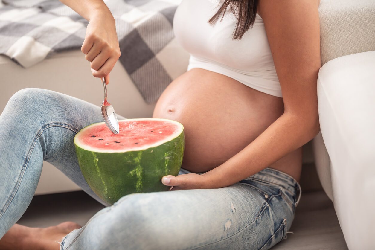 A pregnant woman eating watermelon with a spoon.
