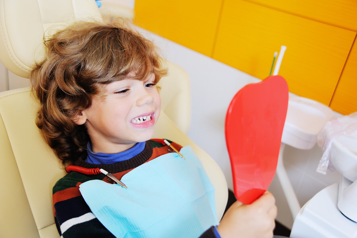 Ett barn i en tandläkarestol som tittar på sina tänder i spegeln.