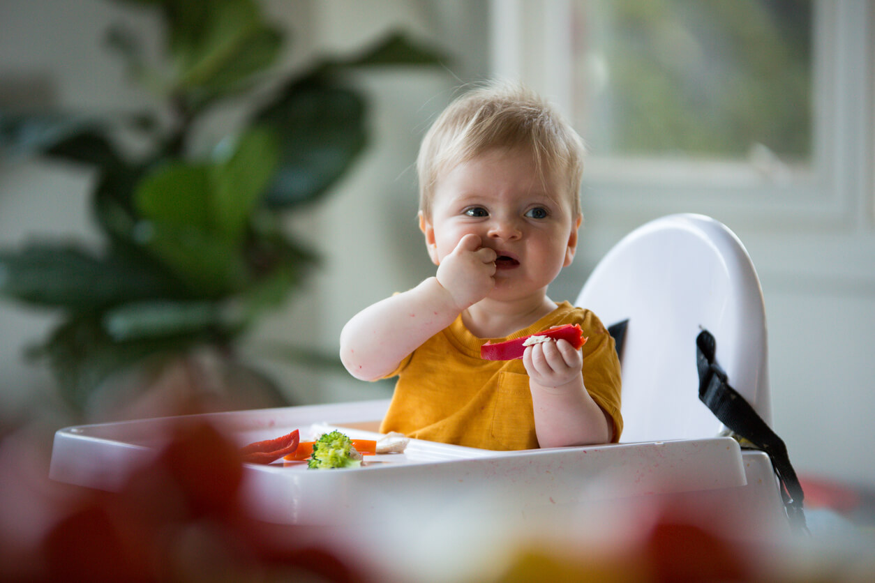 A baby in a high chair eating vegetables.
