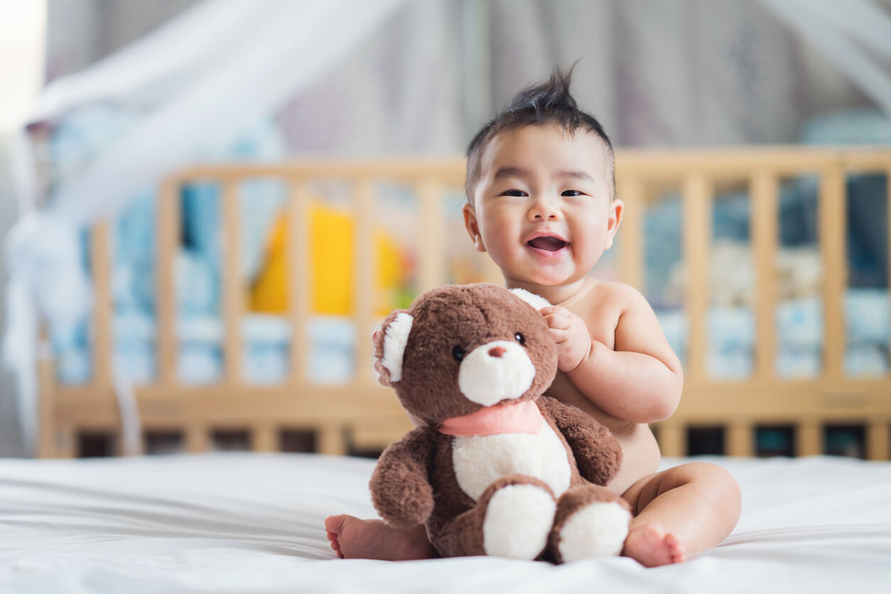 A baby sitting up and smiling while holding a teddy bear.