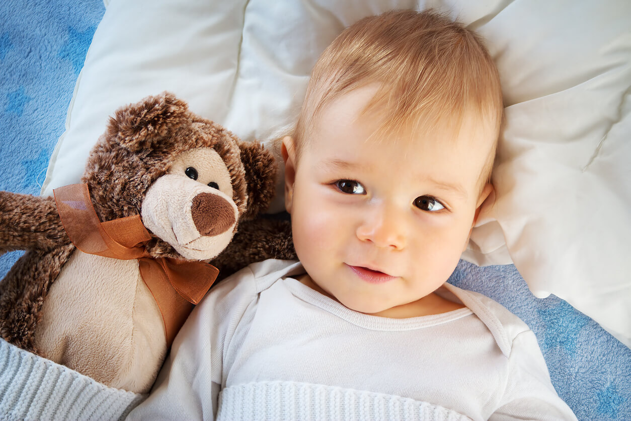 A baby lying in bed next to a teddy bear.