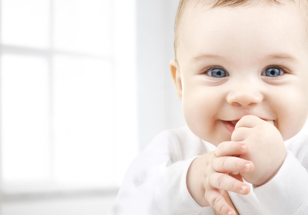 En leende bebis med fingrarna i munnen.