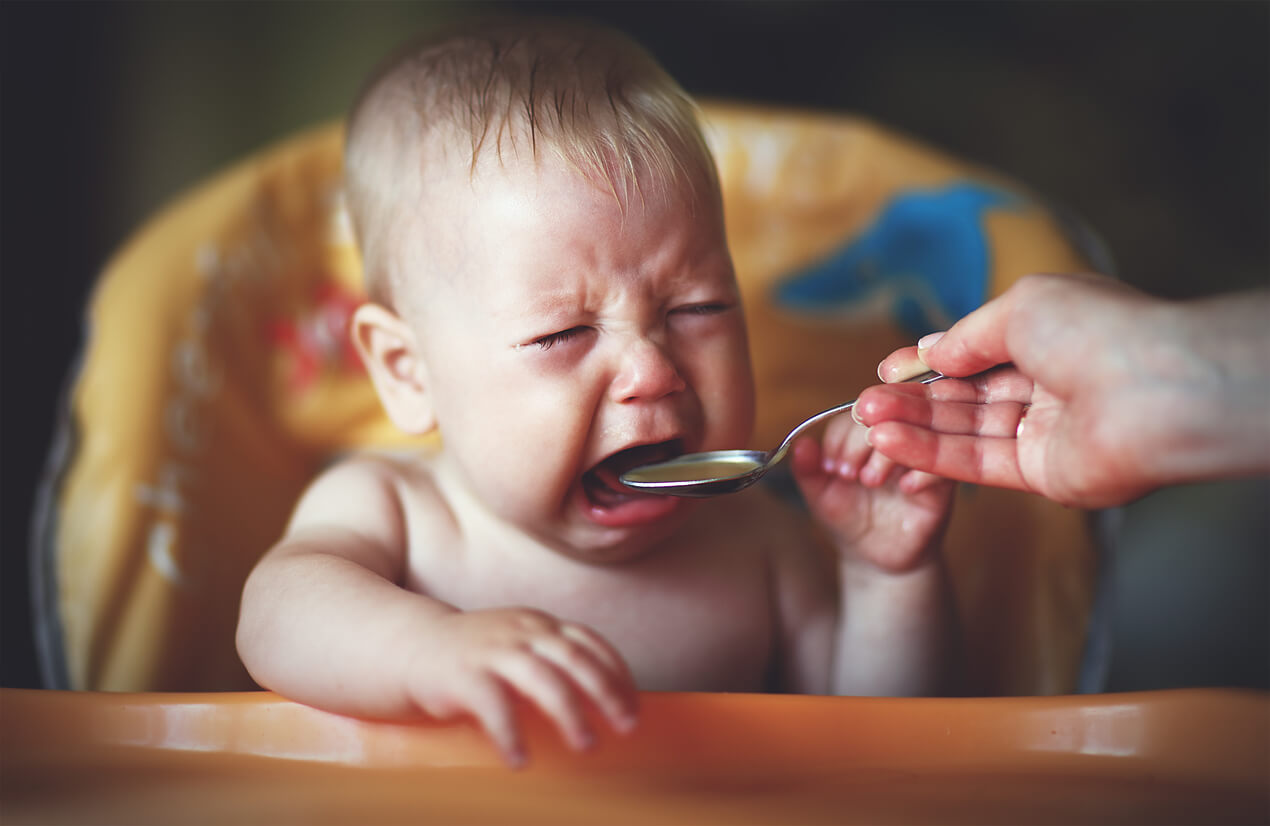 En bebis som gråter medan dess förälder försöker mata den med sked.
