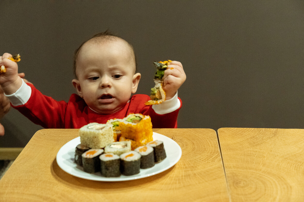 Un bébé qui écrase un sushi dans sa main.