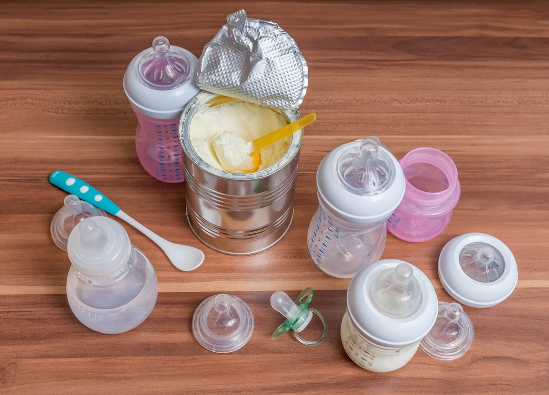 A can of powdered baby formula surrounded by bottles, a pacifier, and a baby spoon.