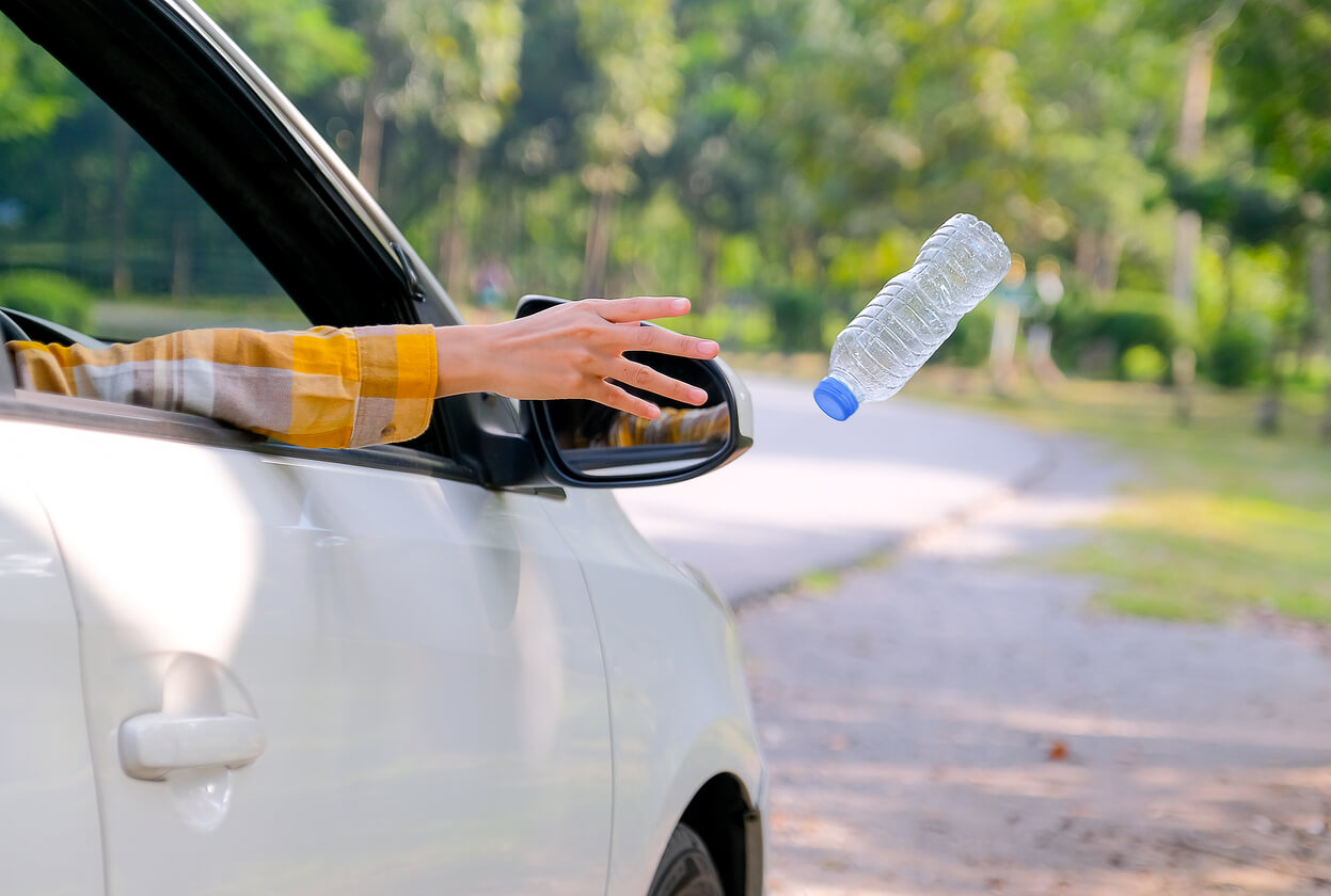 Une personne qui jette une bouteille par la fenêtre de la voiture.