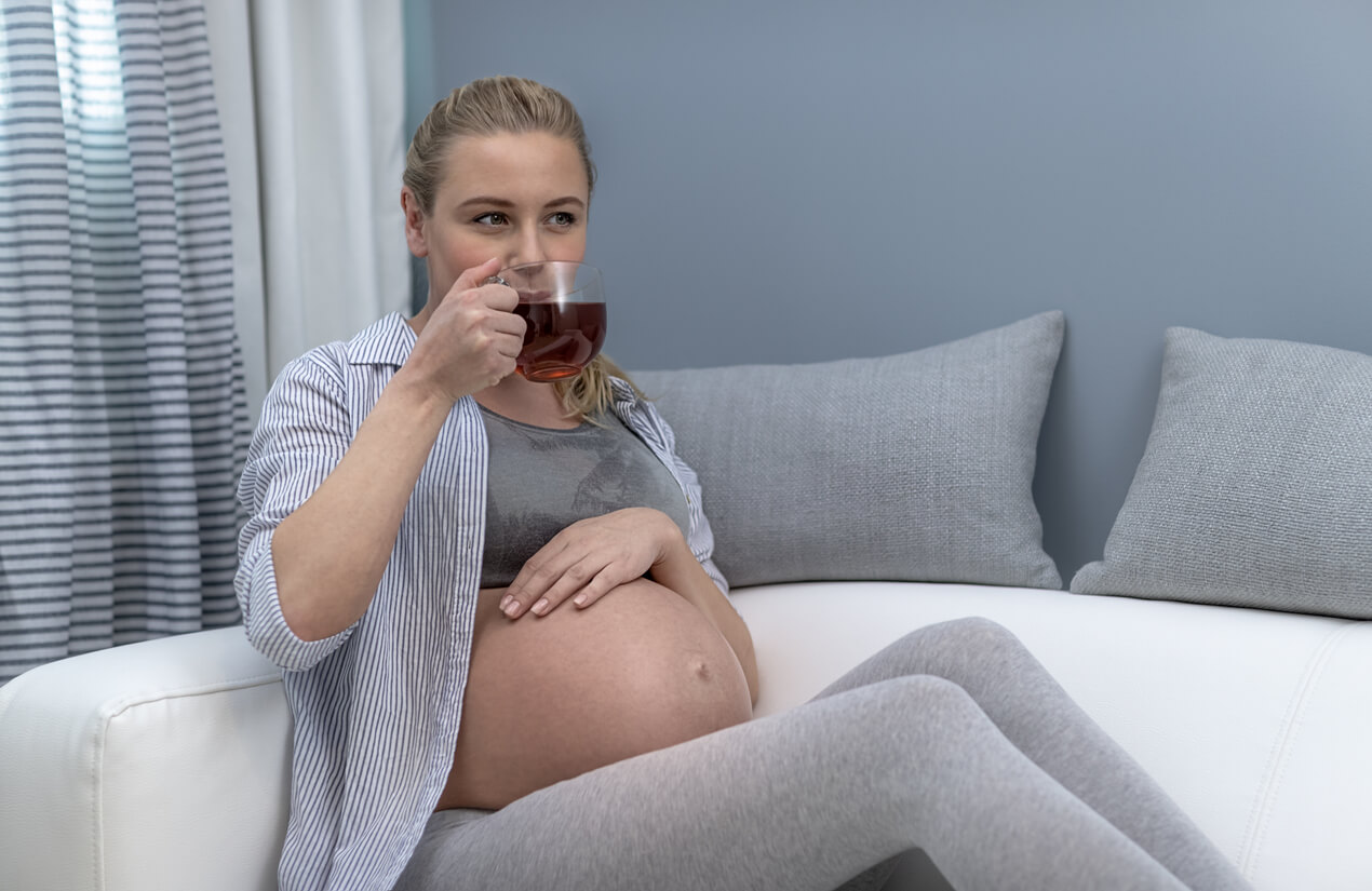 A pregnant woman sitting on the couch drinking tea.
