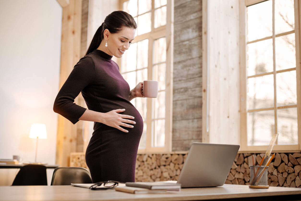 A pregnant woman drinking tea while she works.