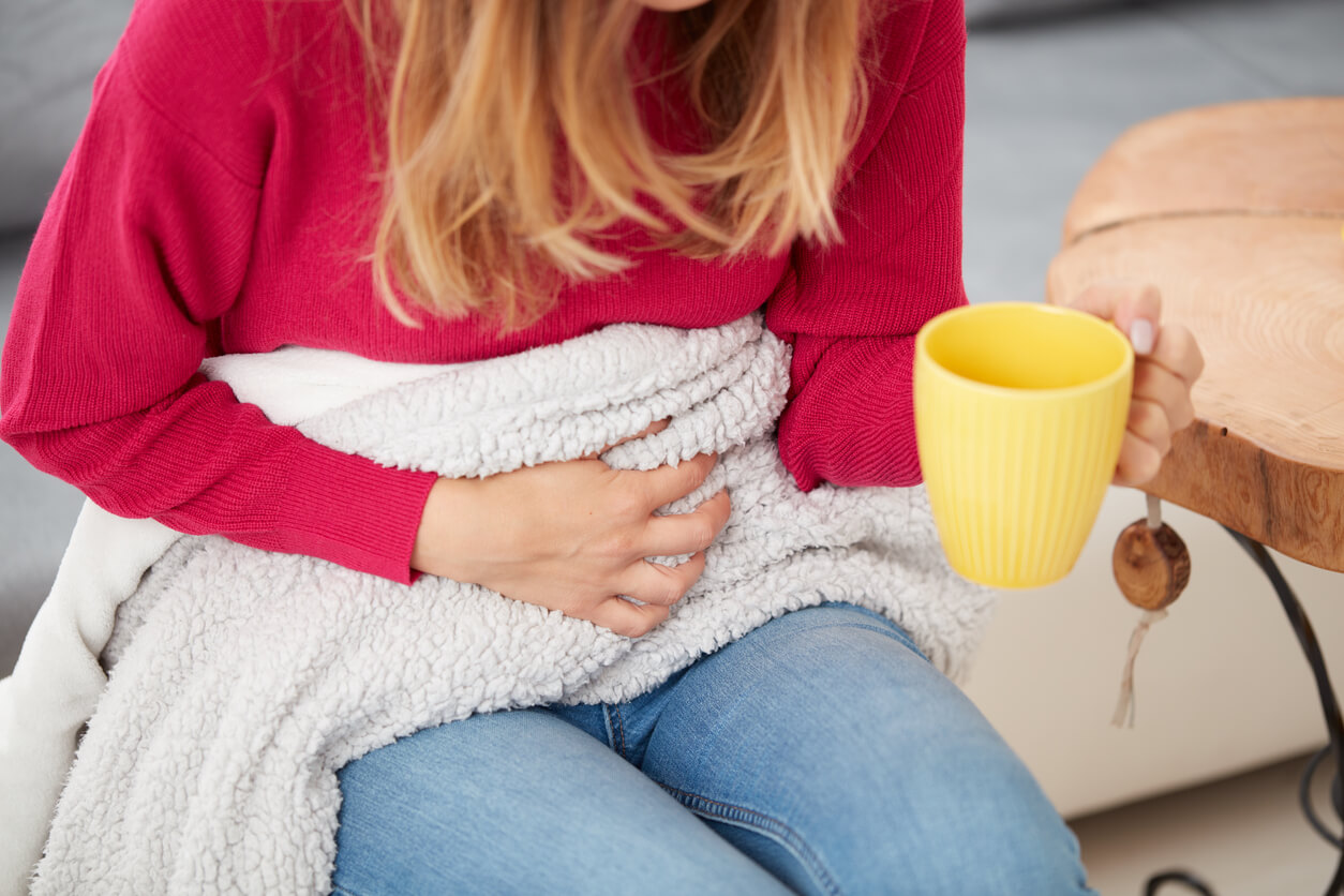 Une femme qui a mal au ventre et boit une infusion.
