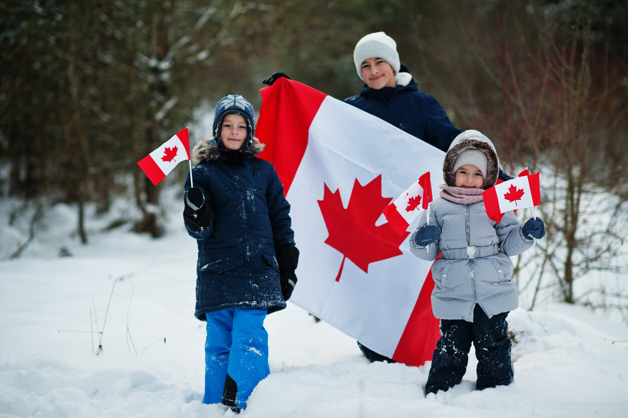 Three children standing in the snow, holding Canadian flags.