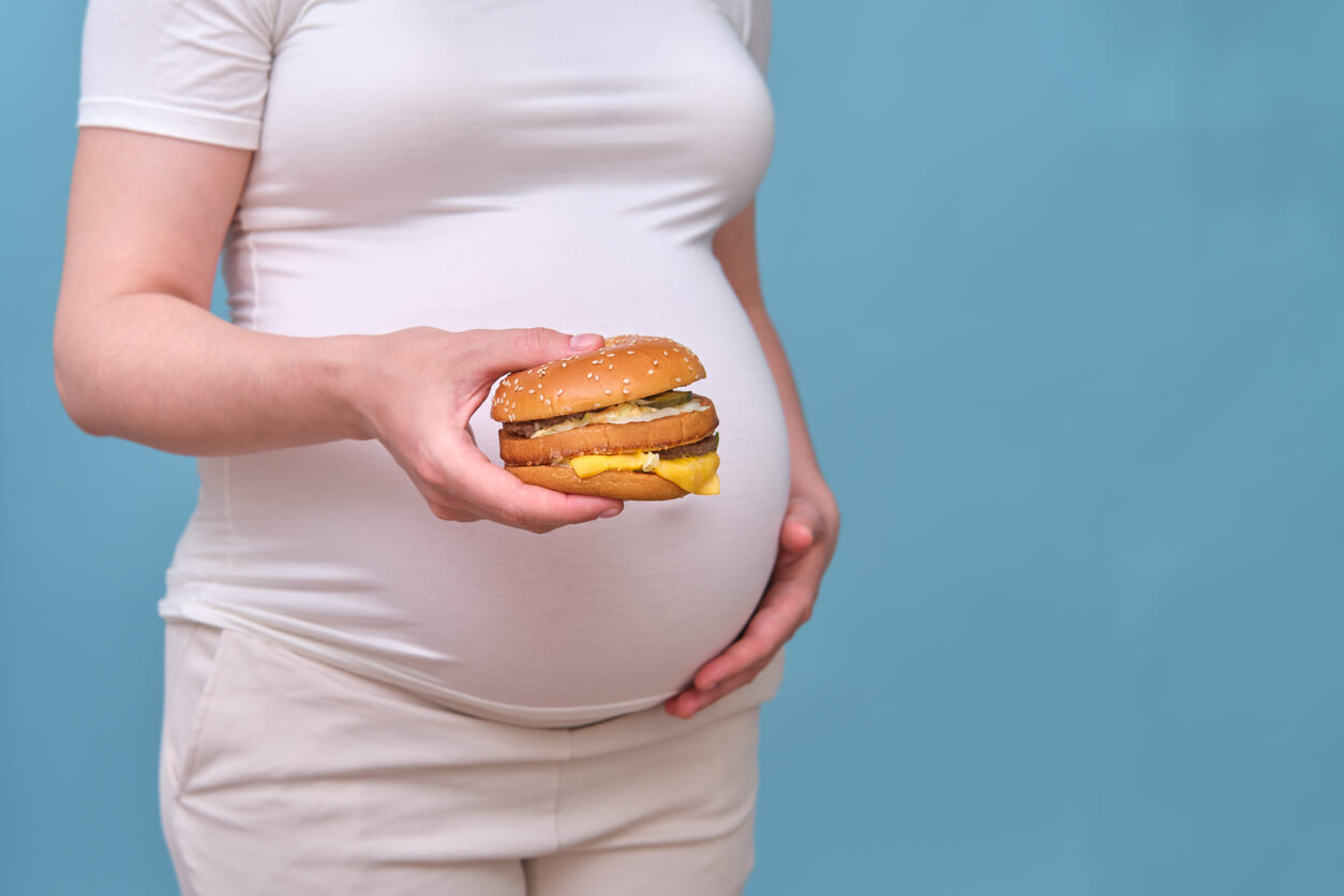 A pregnant woman holding a fast-food cheeseburger.