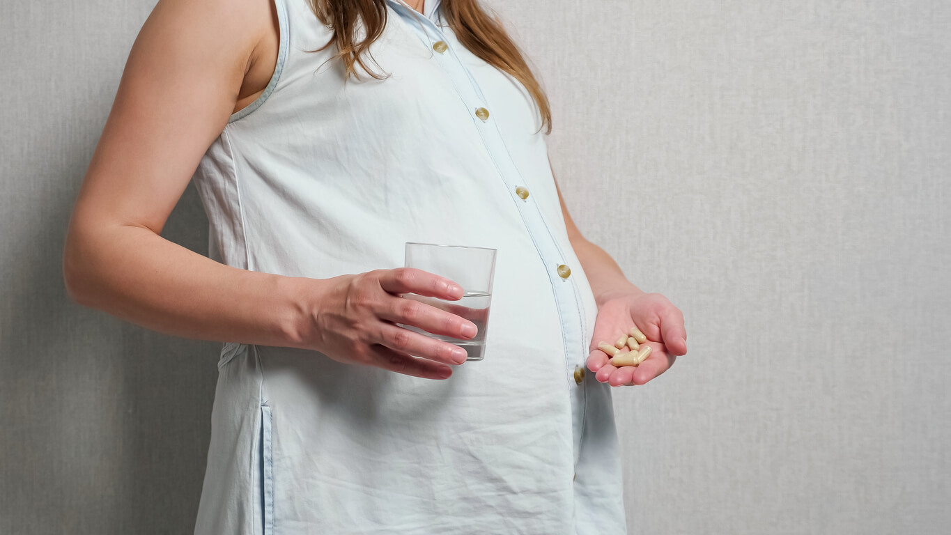 Une femme enceinte avec un verre d'eau et des pastilles dans la main.