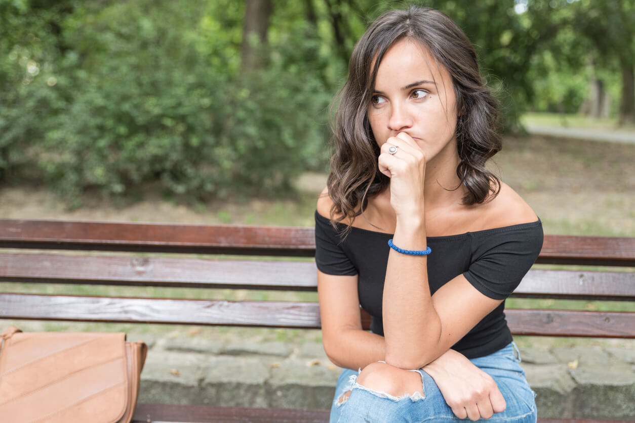 A teenage girl sitting on a park bench looking nervous.