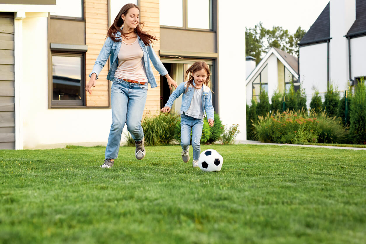 A young mother playing socceer with her daughter in the yard.